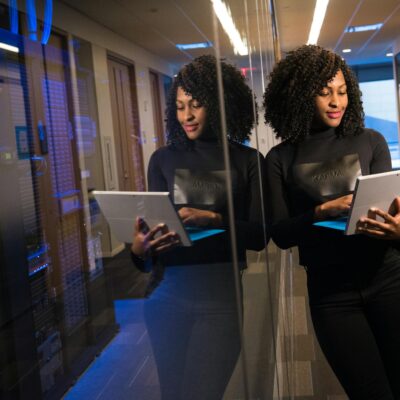 African American woman standing in modern office using laptop, reflecting professionalism and technology engagement.