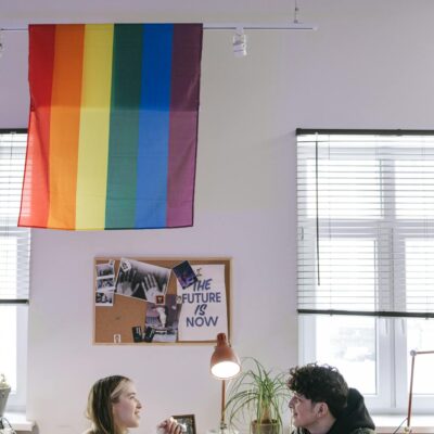 Two colleagues collaborate in a modern workspace with a pride flag displayed.